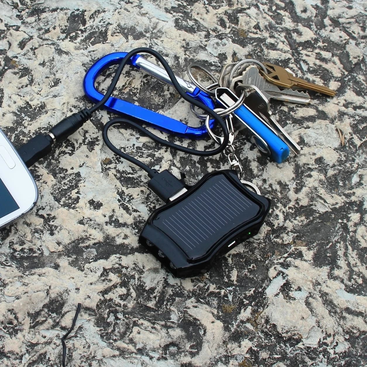 The power bank on a rock with keys on its carabiner, connected to a phone